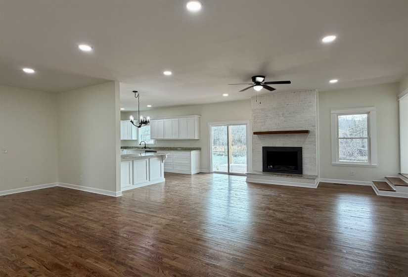 Unfurnished living room with dark wood-type flooring, a large fireplace, suspended lighting, and ceiling fan