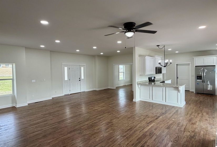 Unfurnished living room with a ceiling fan, hanging lights, and dark wood-style floors