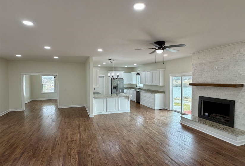 Unfurnished living room with dark wood-style flooring, a brick fireplace, suspended lighting, and a ceiling fan