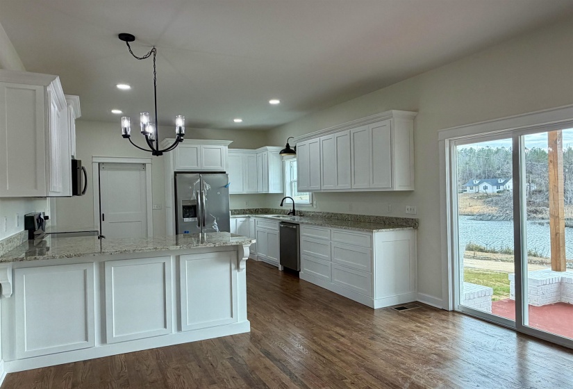 Kitchen featuring white cabinets, light stone counters, stainless steel appliances, a peninsula, and dark wood-style floors