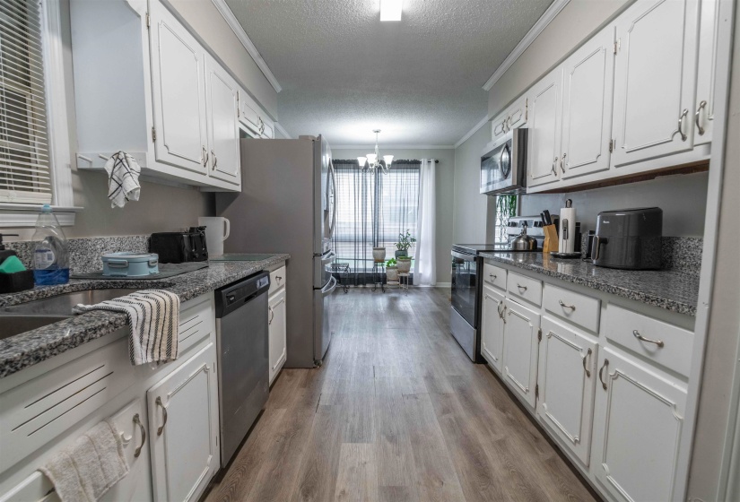 Galley kitchen featuring white cabinetry, speckled countertops, stainless steel appliances, and wood-finish flooring