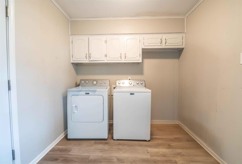Dedicated laundry space featuring white upper cabinetry, light-toned walls, and wood-finish flooring