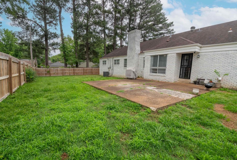 Expansive backyard featuring a concrete patio, wood privacy fencing, and mature trees in the background