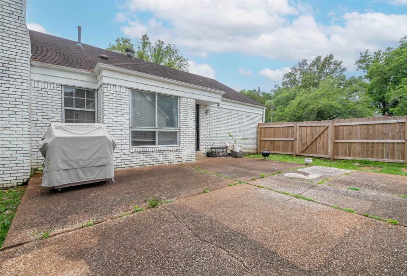 Spacious concrete patio extending from a white brick exterior, bordered by a wood privacy fence and mature trees