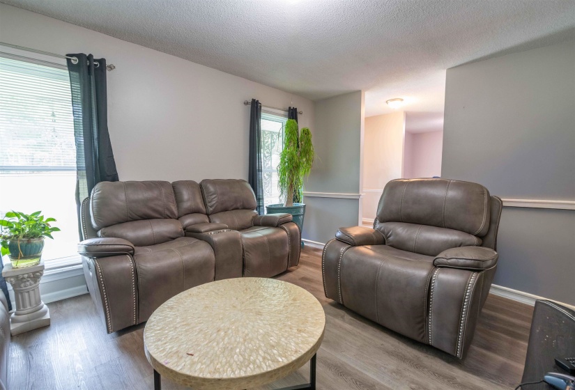 Living area featuring wood-finish flooring, two windows with blinds, and white baseboards with chair railing