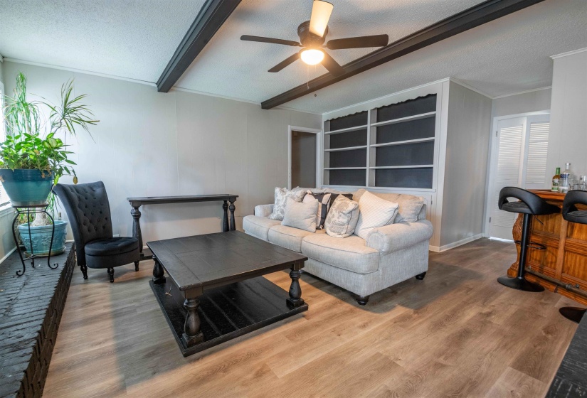 Spacious living area featuring wood-finish flooring, exposed ceiling beams, and a built-in bookshelf