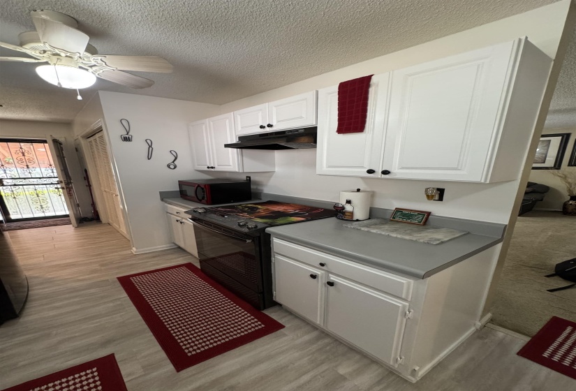 Kitchen featuring white cabinetry with black hardware, gray countertops, a black range, and light wood-finish flooring