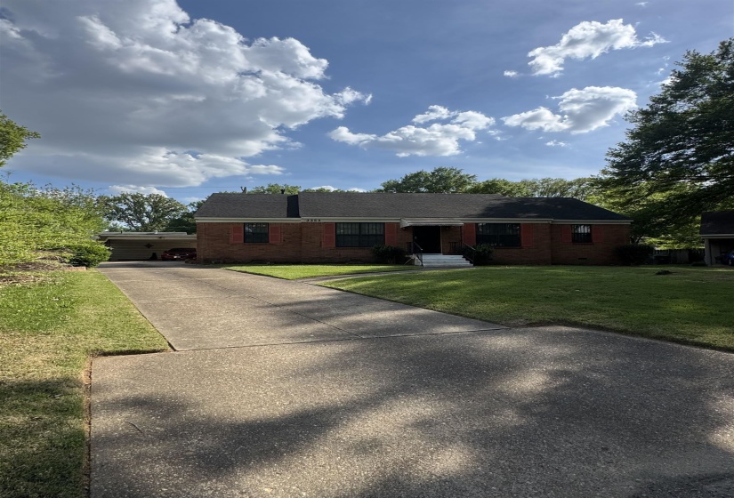 Brick exterior residence featuring a front lawn, mature trees, and a concrete driveway