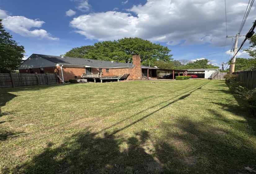 Expansive backyard featuring a manicured lawn, brick exterior, a multi-level deck, a covered patio, and a detached garage