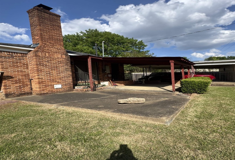 Brick exterior with a prominent chimney, concrete patio area, and a covered carport structure