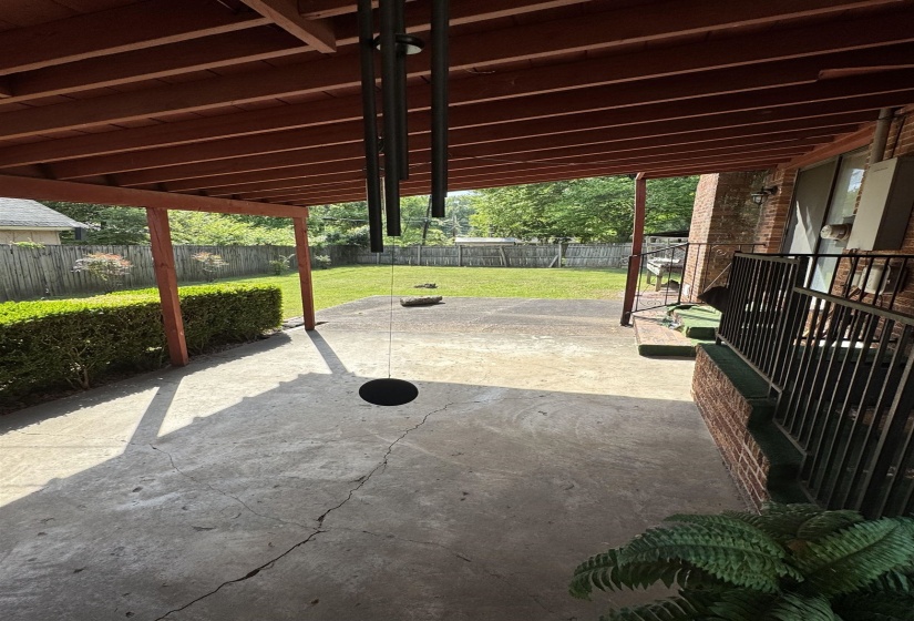Covered concrete patio with exposed rafters and a spacious grass yard bordered by a wooden privacy fence