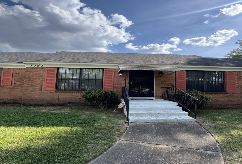 Brick exterior featuring red window shutters, a front entry awning, and a concrete pathway leading to the porch