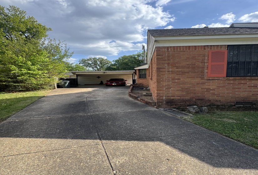 Brick exterior featuring a covered carport, concrete driveway, and red louvered shutters