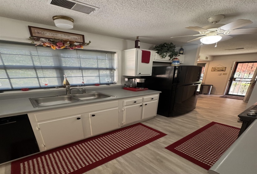 Kitchen featuring light wood-finish flooring, white cabinetry with dark hardware, a double basin stainless steel sink, and a dark refrigerator