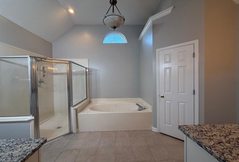 Bathroom featuring a jetted tub, glass-enclosed shower, vaulted ceiling, and recessed lighting