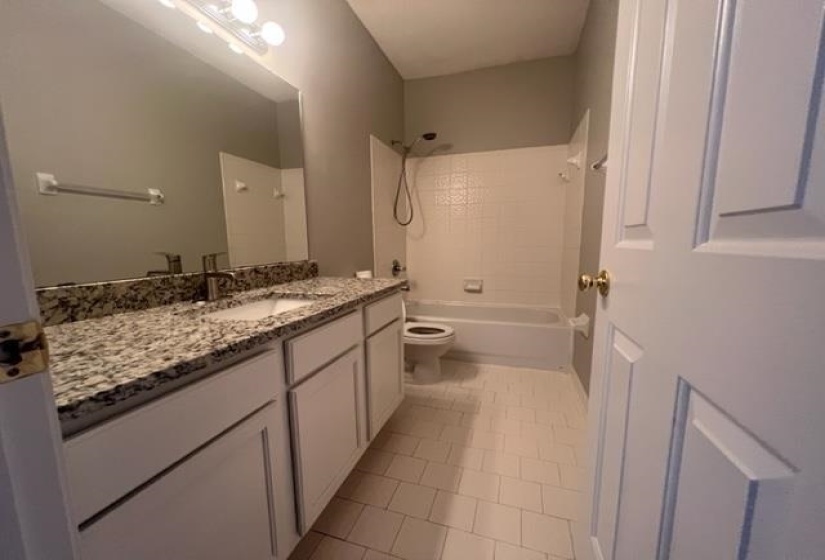 Bathroom featuring a full vanity with an integrated sink, patterned stone countertop, and white shaker-style cabinetry