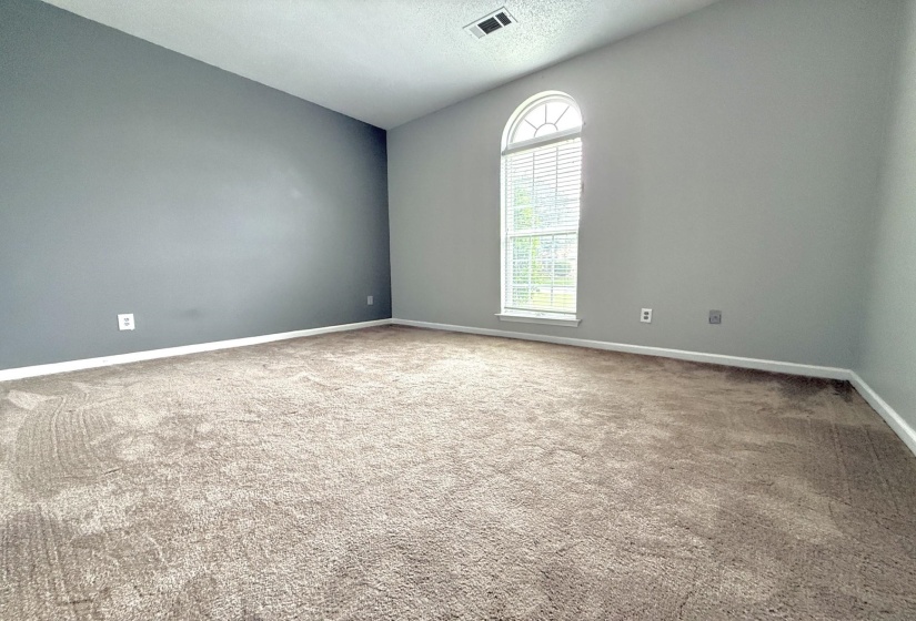 Spacious room featuring neutral carpet flooring and a prominent arched window with louvered blinds