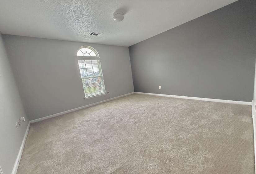 Spacious room featuring neutral carpeting, a vaulted ceiling, and an arched window with horizontal blinds