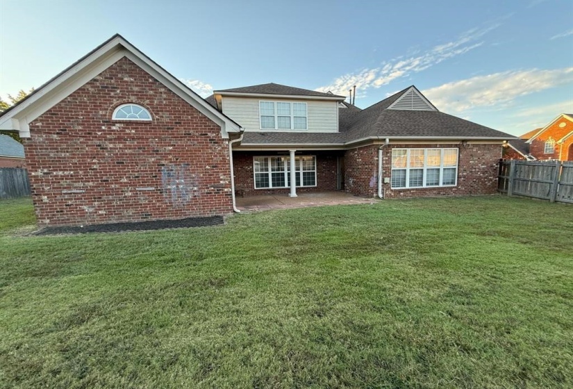 Expansive green lawn bordering a brick and siding exterior with a covered patio area