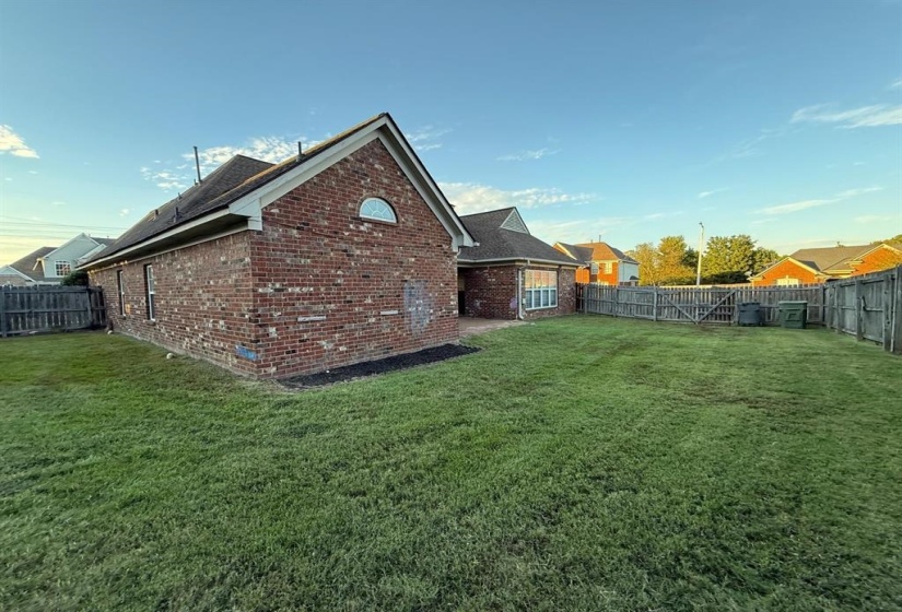 Expansive backyard featuring a manicured lawn, full wood privacy fencing, and a brick exterior with a gable roofline