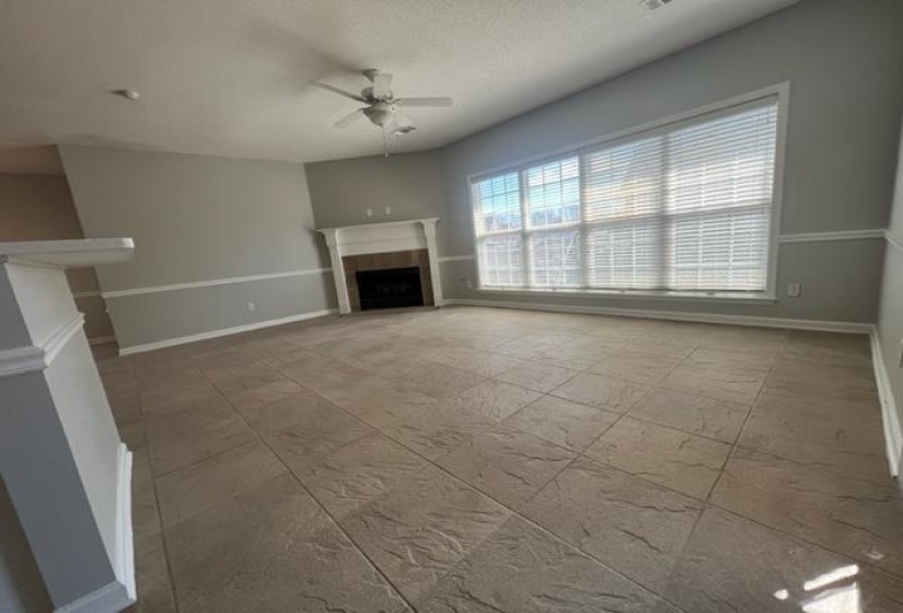 Spacious living area featuring large-format tile flooring, a prominent fireplace with a white mantel, and extensive window coverage