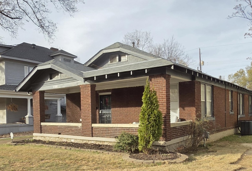 View of side of property with covered porch, brick siding, and a lawn