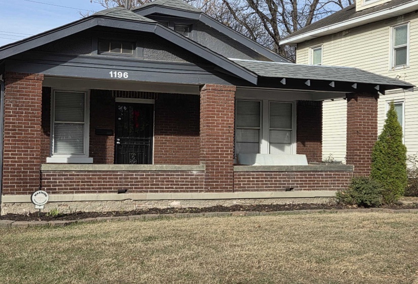 View of exterior entry with covered porch, a yard, and brick siding