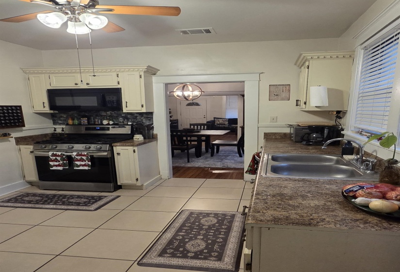 Kitchen with stainless steel range with gas cooktop, light tile patterned floors, black microwave, ceiling fan, and dark countertops