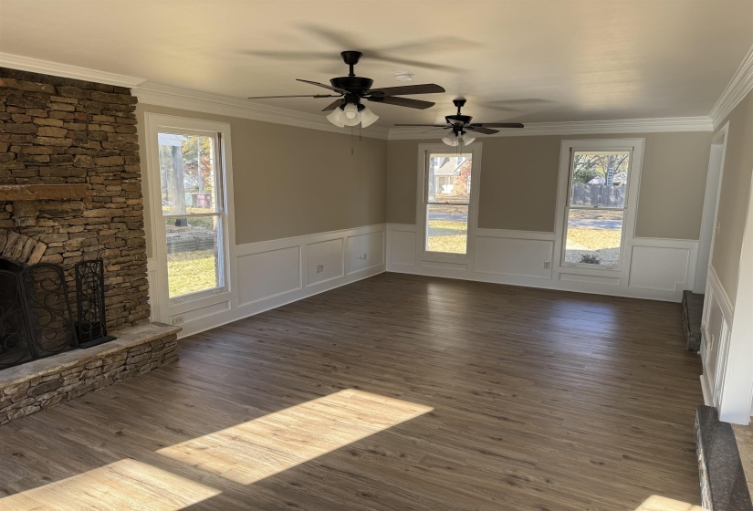 Unfurnished living room featuring a stone fireplace, crown molding, and dark hardwood / wood-style flooring