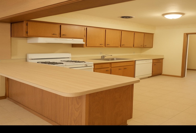 Kitchen featuring white appliances, a peninsula, under cabinet range hood, light countertops, and brown cabinetry