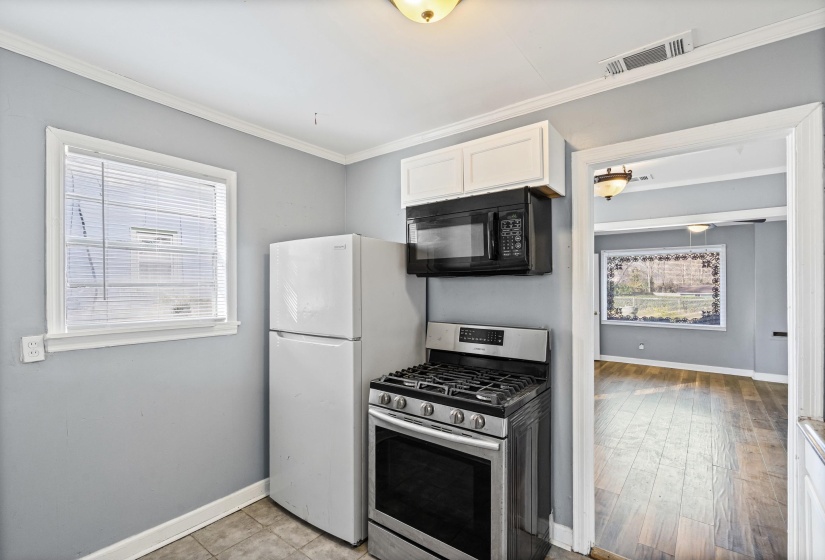 Kitchen with gas stove, black microwave, ornamental molding, white cabinets, and freestanding refrigerator