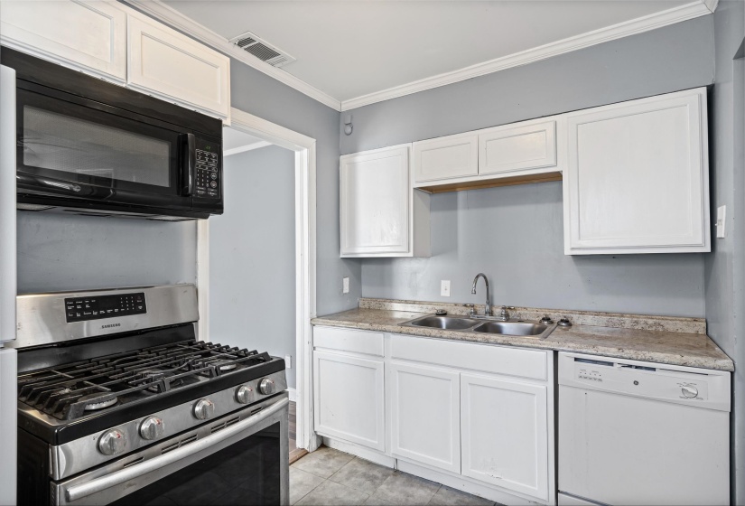 Kitchen featuring stainless steel range with gas stovetop, dishwasher, black microwave, white cabinets, and light countertops