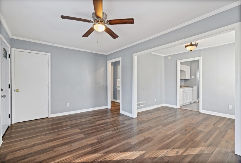Unfurnished living room featuring ornamental molding, dark wood-type flooring, and a ceiling fan