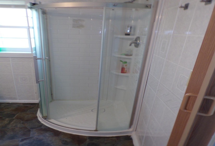 Bathroom featuring a shower stall, dark stone finish floors, and tile walls