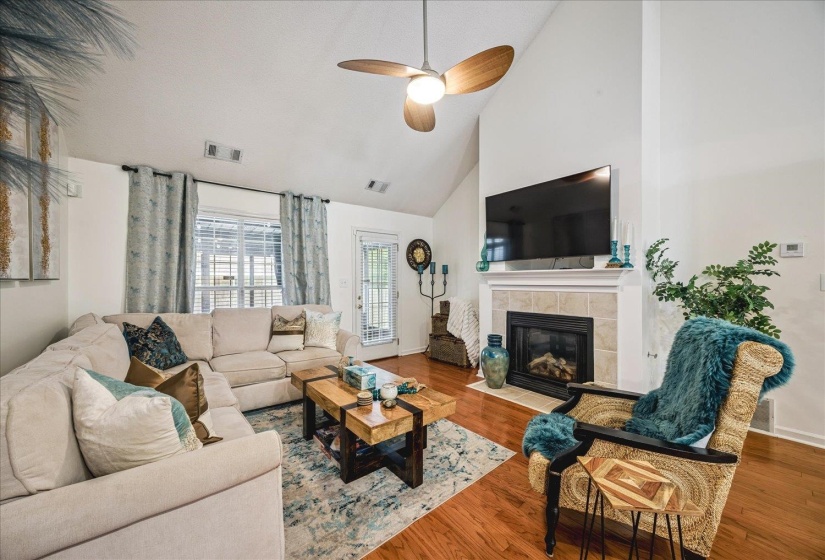 Living area featuring vaulted ceilings, a fireplace with a tile surround, wood-finish flooring, and a ceiling fan