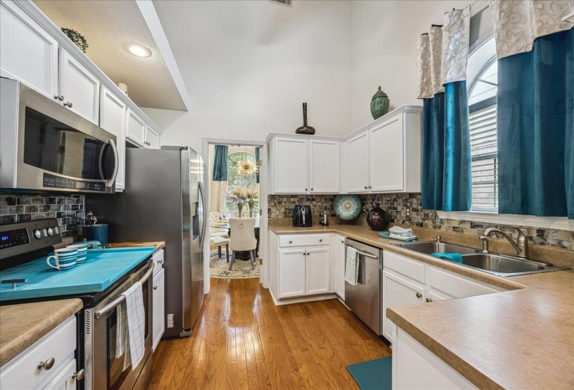 Kitchen featuring white cabinetry, stainless steel appliances, a mosaic tile backsplash, wood-finish flooring, and a vaulted ceiling
