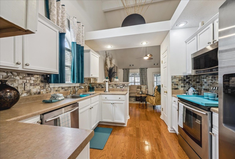 Modern kitchen featuring white cabinetry, light countertops, wood-finish flooring, a mosaic tile backsplash, and stainless steel appliances