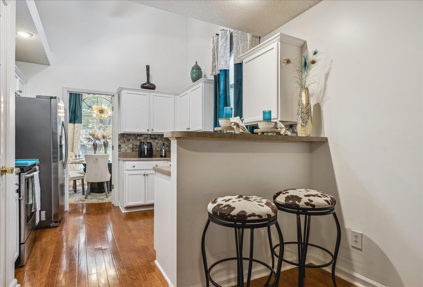 Kitchen featuring white cabinetry, light countertops, mosaic tile backsplash, wood-finish flooring, and a breakfast bar