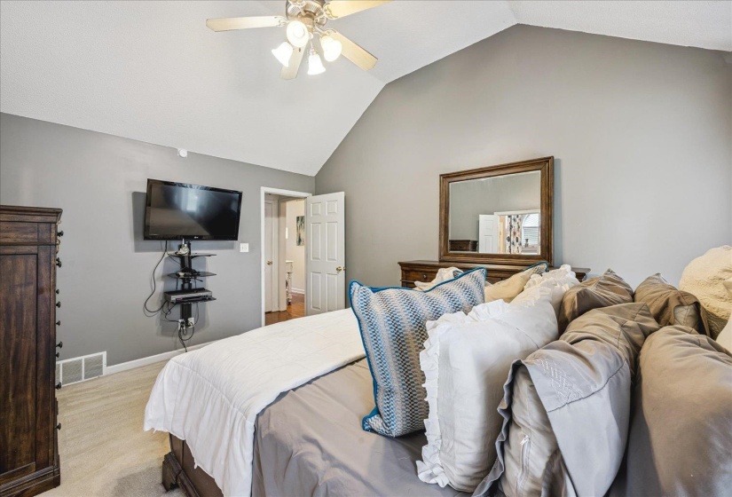 Vaulted ceiling bedroom with a ceiling fan, light gray wall color, and light-toned carpet flooring
