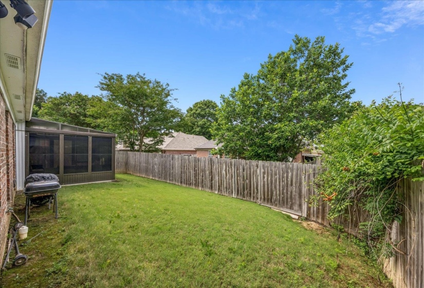 Spacious backyard featuring a screened patio, a wood privacy fence, and mature perimeter trees