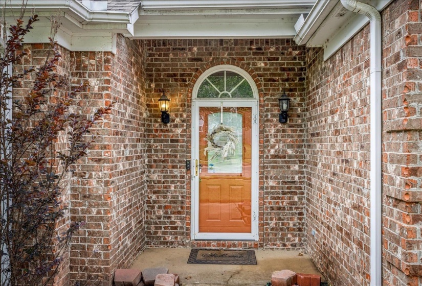 Brick exterior entry featuring a wood-finish door with an arched transom, glass paneling, and two sconce lights