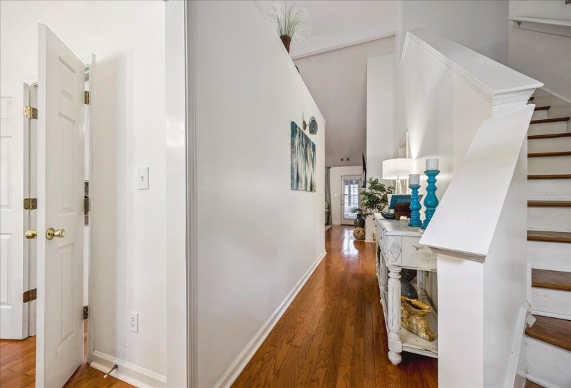 Hardwood flooring throughout the main corridor, featuring white walls, vaulted ceilings, and a staircase with painted risers and wood treads