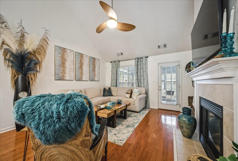 Vaulted ceiling living space with wood-finish flooring, a fireplace featuring a tiled surround and hearth, and a contemporary ceiling fan