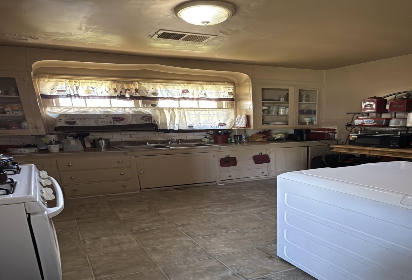 Kitchen featuring a double basin sink with window, upper and lower cabinetry, and tile flooring