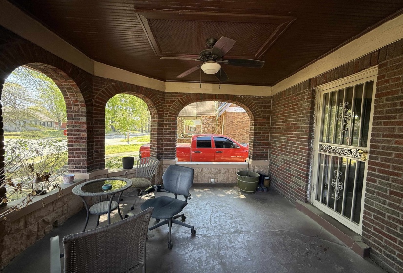 Covered brick porch featuring multiple archways, a dark wood-finish ceiling with a ceiling fan, and a security screen door