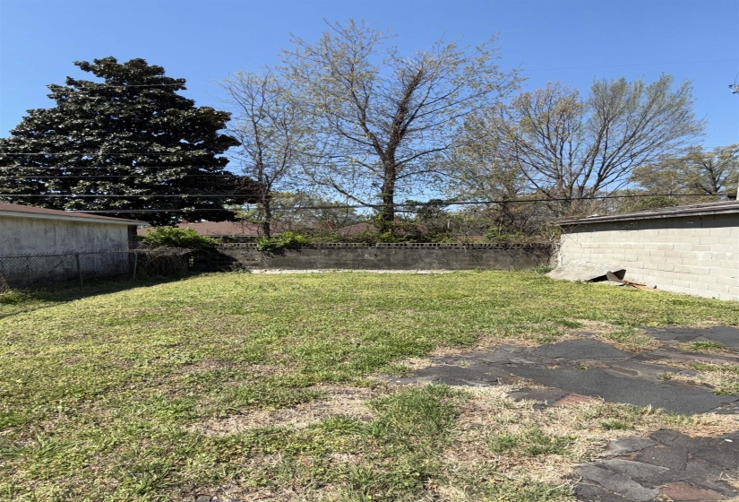 Grassed yard area featuring a concrete block retaining wall and partial asphalt paving