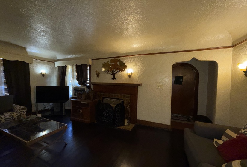 Living area featuring dark wood-finish flooring, a fireplace with a wood mantel, an arched entry, and wall sconce lighting