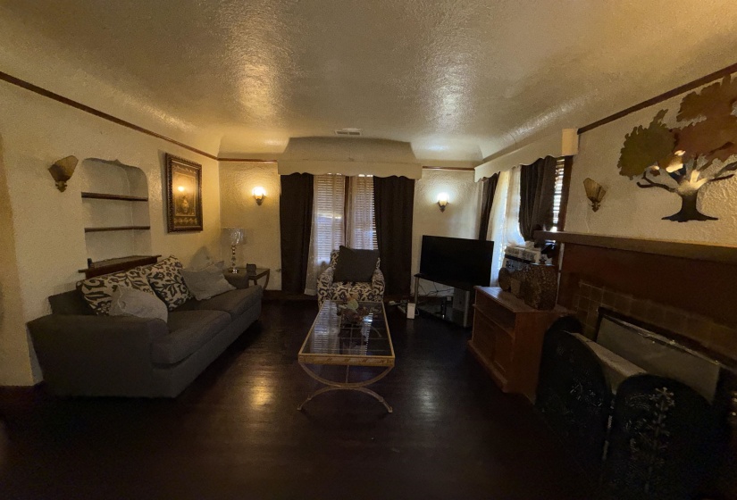 Living area featuring dark wood-finish flooring, textured walls, built-in shelving, two wall sconces, and a fireplace with decorative tile work