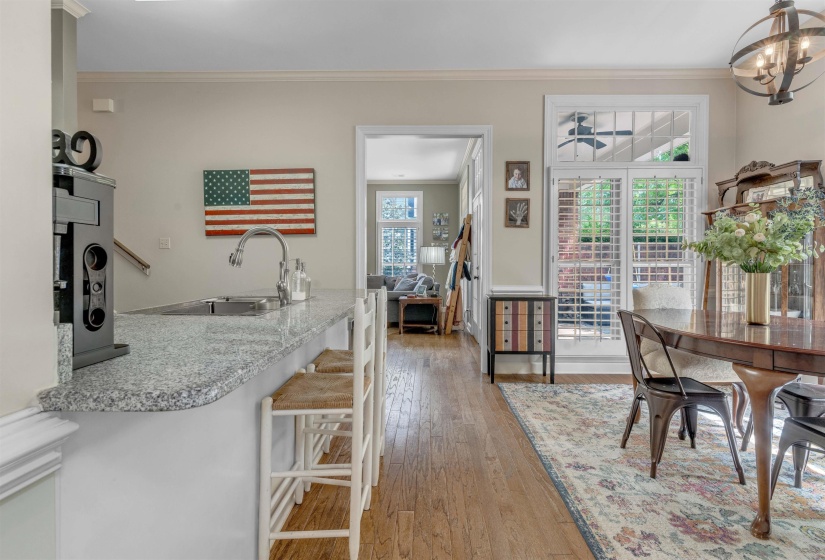 Granite countertop island with undermount sink, hardwood flooring, crown molding, and plantation shutters
