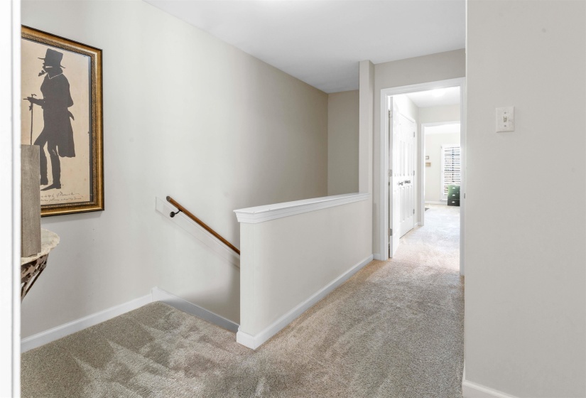 Carpeted hallway with a painted half-wall railing and a wood handrail